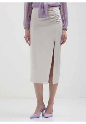 Femme portant une jupe crayon midi beige avec une fente latérale et un détail froncé, associée à des talons slingback pointus lavande et une blouse.