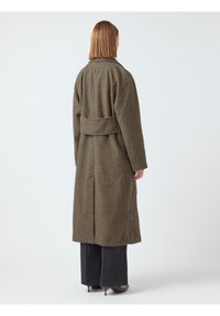 Abrigo largo de cuadros houndstooth marrón, con cinturón en la cintura, corte ligeramente holgado y una tela texturizada. Incluye una abertura trasera para mayor movilidad.