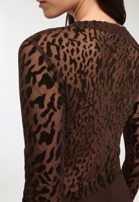 Top trasparente marrone con un motivo in stampa leopardata testurizzata di un marrone più scuro, maniche lunghe e scollo rotondo. Tessuto morbido e elasticizzato.