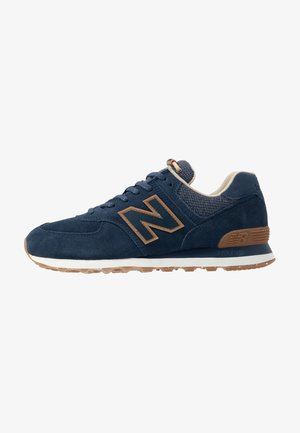 Marineblaue New Balance Sneaker mit braunem Logo und Akzenten, weißer Mittelsohle, Kautschukaußensohle sowie einem Obermaterial aus Stoff und Wildleder.