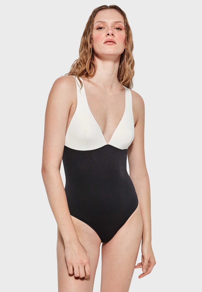 Bañador de una pieza en blanco y negro con un escote en V profundo. Hecho de una tela suave, con tirantes anchos y una silueta ajustada.