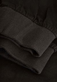 Tela negra con puños acanalados, que muestra múltiples capas y una textura suave. Diseño simple sin patrones ni acentos.