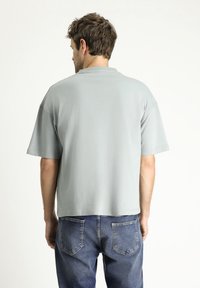 Camiseta de gran tamaño en gris claro con mangas cortas, cuello redondo y una textura suave, combinada con jeans de mezclilla azul.