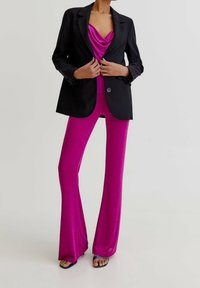 Zwarte blazer over een roze top met cowl-hals en uitlopende broek. De outfit is gemaakt van gladde stof, met een getailleerd silhouet en een blazer met knopen.