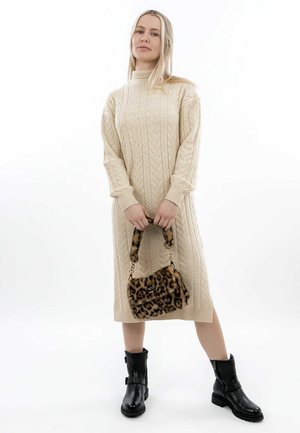 Abito lavorato a maglia beige con scollatura alta e motivo a treccia; abbinato a una borsa in pelliccia con stampa leopardo e stivali neri alla caviglia.