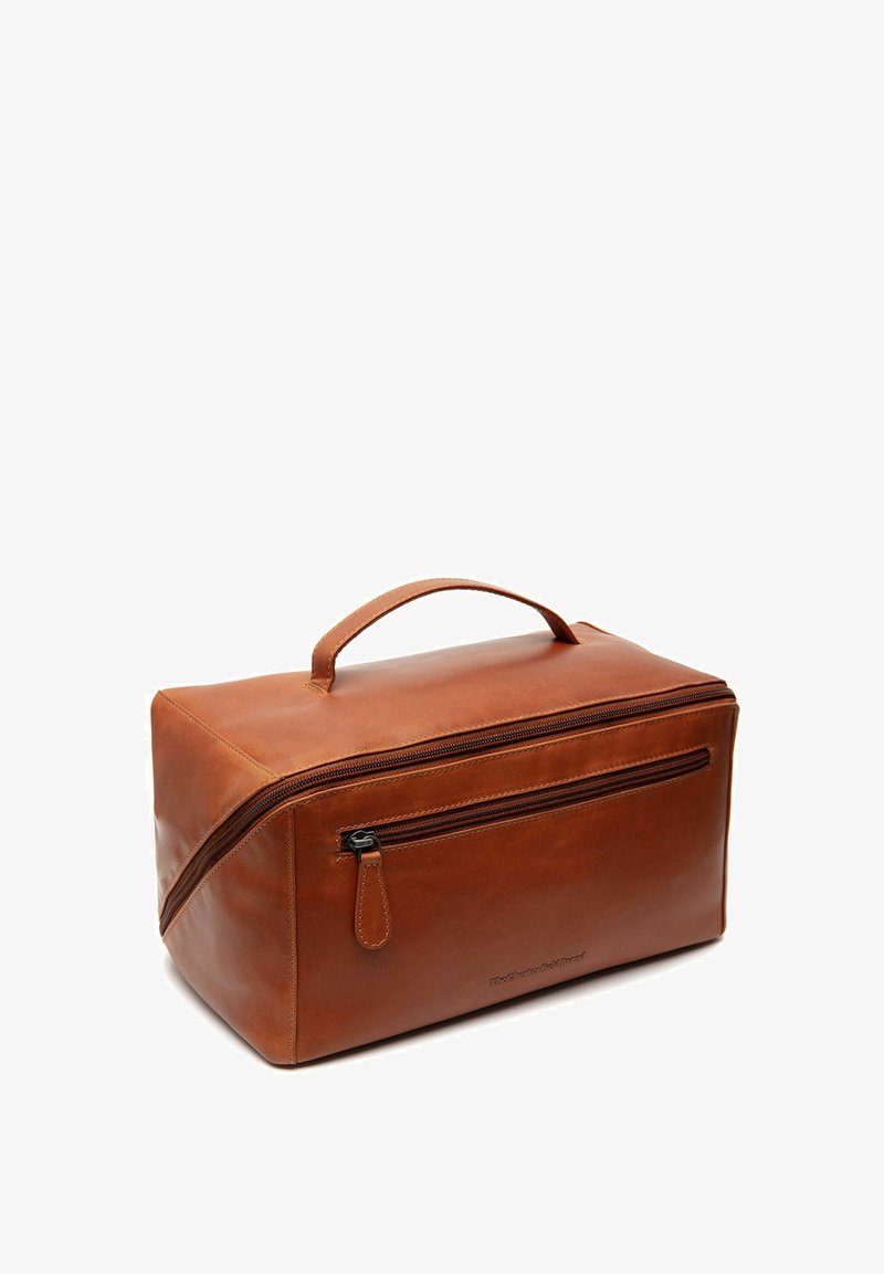 Trousse de toilette en cuir marron avec une forme rectangulaire, une poignée supérieure et une poche zippée à l'avant. Texture lisse avec des détails de coutures visibles.