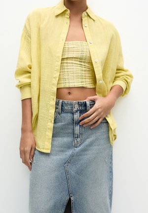 Person iført en gul skjorte med knapper over en gul ternet tube-top og en lyseblå denim nederdel med slids foran.