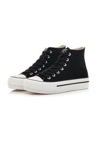 Zapatillas altas negras de lona con suelas de goma blanca, punteras y un acento de rayas negras a lo largo de la suela. Diseño con cordones.