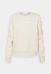 Béžová mikina s kulatým výstřihem a textem "Calvin Klein Jeans" umístěným na středu hrudníku, s malým vyšitým logem "CK" na manžetě levého rukávu.