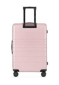 Jasnoróżowa walizka o błyszczącym wykończeniu, z wysuwaną czarną rączką, kółkami do toczenia oraz poziomymi rowkami na powierzchni dla zwiększenia tekstury.