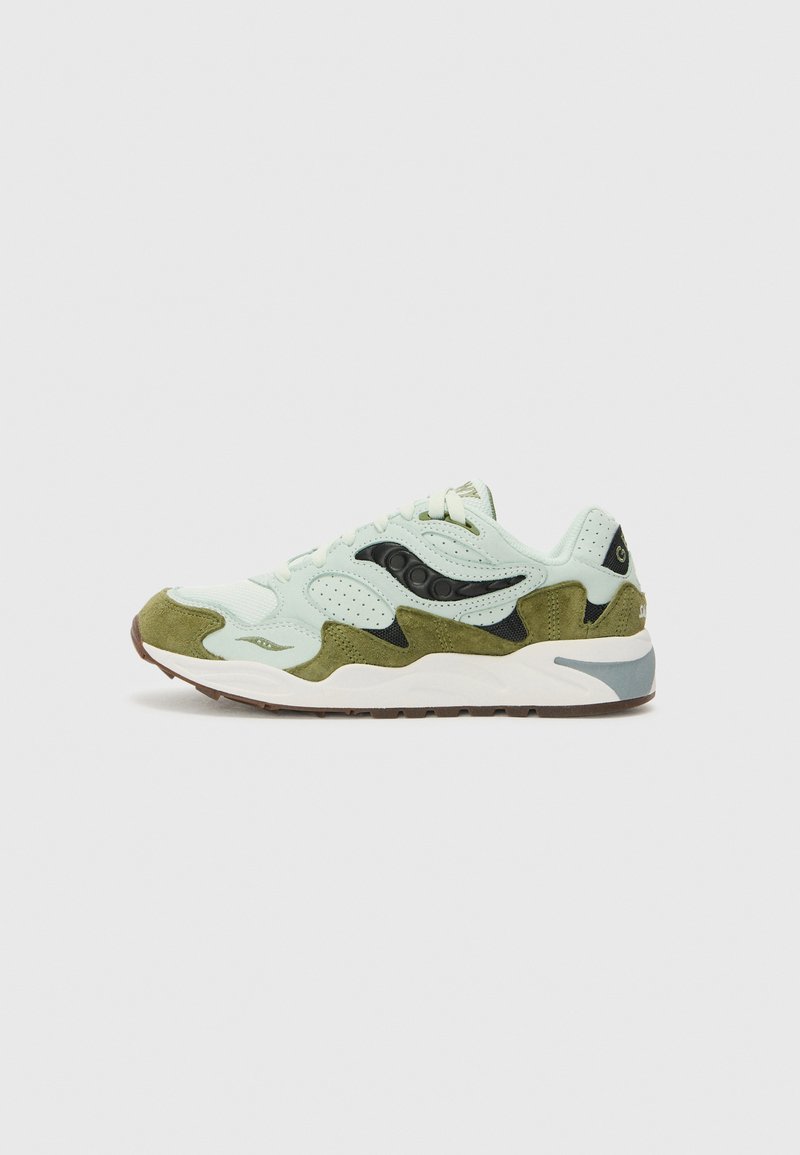Zapatilla de ante en verde claro y oliva con acentos en negro, suela blanca y suela de goma marrón, mostrada de lado sobre un fondo plano.