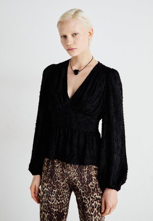 Black textured blouse with puffy sleeves and a V-neck, paired with brown leopard-print pants. Features pleating and a peplum style.