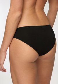 Mutande bikini in cotone nero con design senza cuciture, gambe alte e una texture morbida visibile dalla vista posteriore.
