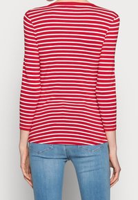 Pitkähihainen punavalkoraidallinen paita, jossa on pyöreä pääntie ja vartalonmyötäinen malli. Materiaali vaikuttaa pehmeältä; takakuvassa näkyy kapea istuvuus ja rento tyyli.
