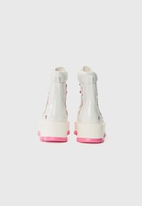 Witte hoge laarzen met glanzende lakafwerking, roze rubberen zool en veters met een subtiel ontwerp. Ronde neus en gevoerde kraag.
