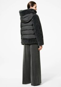 Giacca a vento imbottita di un grigio scuro con un esterno morbido e testurizzato e sezioni trapuntate lisce e gonfie. Presenta un cappuccio e maniche larghe.