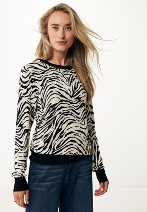 Licht beige trui met zwarte zebra strepen, geribbelde halslijn en manchetten, zachte textuur, gecombineerd met donkerblauwe jeans.