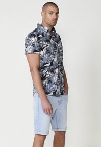 Camicetta a maniche corte nera con motivo tropicale a foglia bianca, abbinata a pantaloni corti in denim azzurri, arrotolati all'orlo. Design casual.