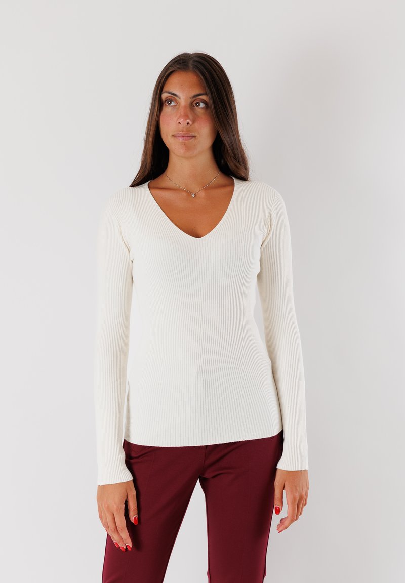 Top a maniche lunghe a coste crema con scollatura a V e silhouette aderente, abbinato a pantaloni bordeaux. Texture liscia, design minimalista.