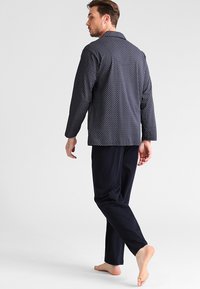 Navy in een patroon pyjama set met een geknoopte blouse met lange mouwen. De blouse heeft een geometrisch ontwerp, gecombineerd met effen donkere broek.