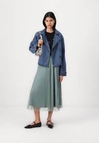 Denim jakna z dvojnimi gumbi, v kombinaciji z nabranim zeleni mint krilom in črnimi balerinkami z očesnimi detajli. Srebrna torbica.