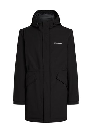 Parka negra impermeable con capucha, cierre de cremallera, ajustadores de traba y bolsillos con botón a presión; textura suave con un diseño minimalista.
