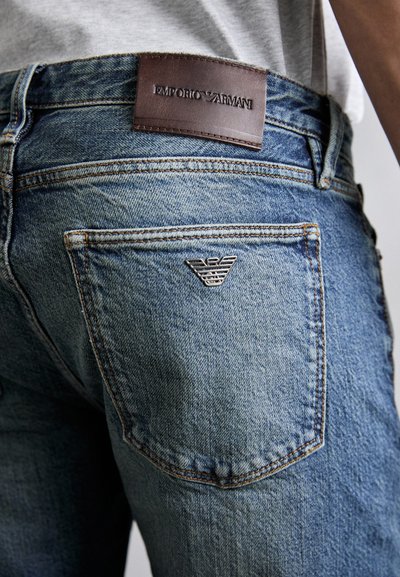 Jeans de denim azul claro com um patch de pele na parte de trás, gravado com "Emporio Armani". Possui detalhes em logo prateado no bolso de trás.