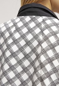 Czarna i biała szachownica z nieregularnym wzorem siatki oraz czarnym kołnierzykiem z tyłu odzieży noszonej przez osobę.