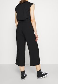 Pantalon culotte noir avec une coupe ajustée, doté d'une taille haute et de plis. Associé à des baskets montantes noires. Texture lisse.