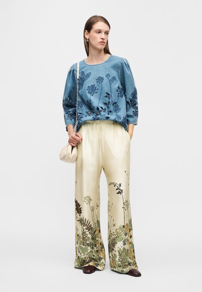Φούτερ από τζιν με κεντήματα λουλουδιών, συνδυασμένο με κρεμ παντελόνι φαρδιάς γραμμής με βοτανικά σχέδια. Περιλαμβάνει μικρό κρεμ τσαντάκι.