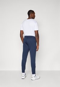 Navy Jogginghosen mit elastischem Bund und Bündchen, kombiniert mit einem schlichten weißen T-Shirt, getragen mit weißen Sportschuhen.