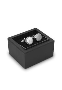 Srebrne spinki do mankietów o okrągłym wzorze i wygrawerowanym logo, prezentowane w czarnej pudełku z czarnym welurowym wykończeniem.