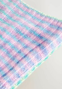 Couverture en tricot avec des nuances de rose pastel, bleu et vert ; elle présente un motif en damier texturé avec des bords frangés. Tissu doux et léger.