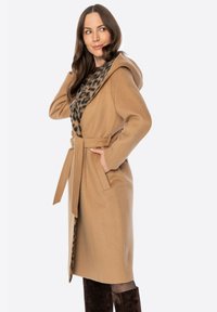 Beżowy płaszcz zapinany na zamek z kapturem, paskiem do wiązania i podszewką w panterkę. Wykonany z miękkiego materiału, z długimi rękawami i luźnym krojem.