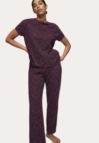 Lilla pyjamas sæt med en kortærmet skjorte og lange bukser med et prikket mønster i pink. Blødt stof og afslappet pasform forbedrer komforten.