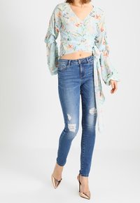 Svetle modrý květinový zavinovací top s dlouhými zvonovými rukávy, v kombinaci s roztrhanými modrými skinny džíny a metalickými vysokými podpatky.