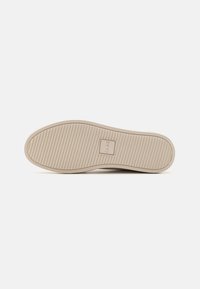 Suola di scarpa in gomma color beige con un motivo testurizzato e rigato. Presenta un logo quadrato al centro che indica il nome del brand "CLAE."