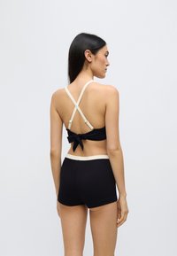 Svart ribbestrikket bikinitopp med knute bak, med kremfargede kryssende stropper bak. Matchende svarte ribbestrikkede shorts med kremfarget linning.