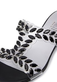 Clear slide sandal featuring a black and transparent design adorned with black oval crystals, resting on a black sole.