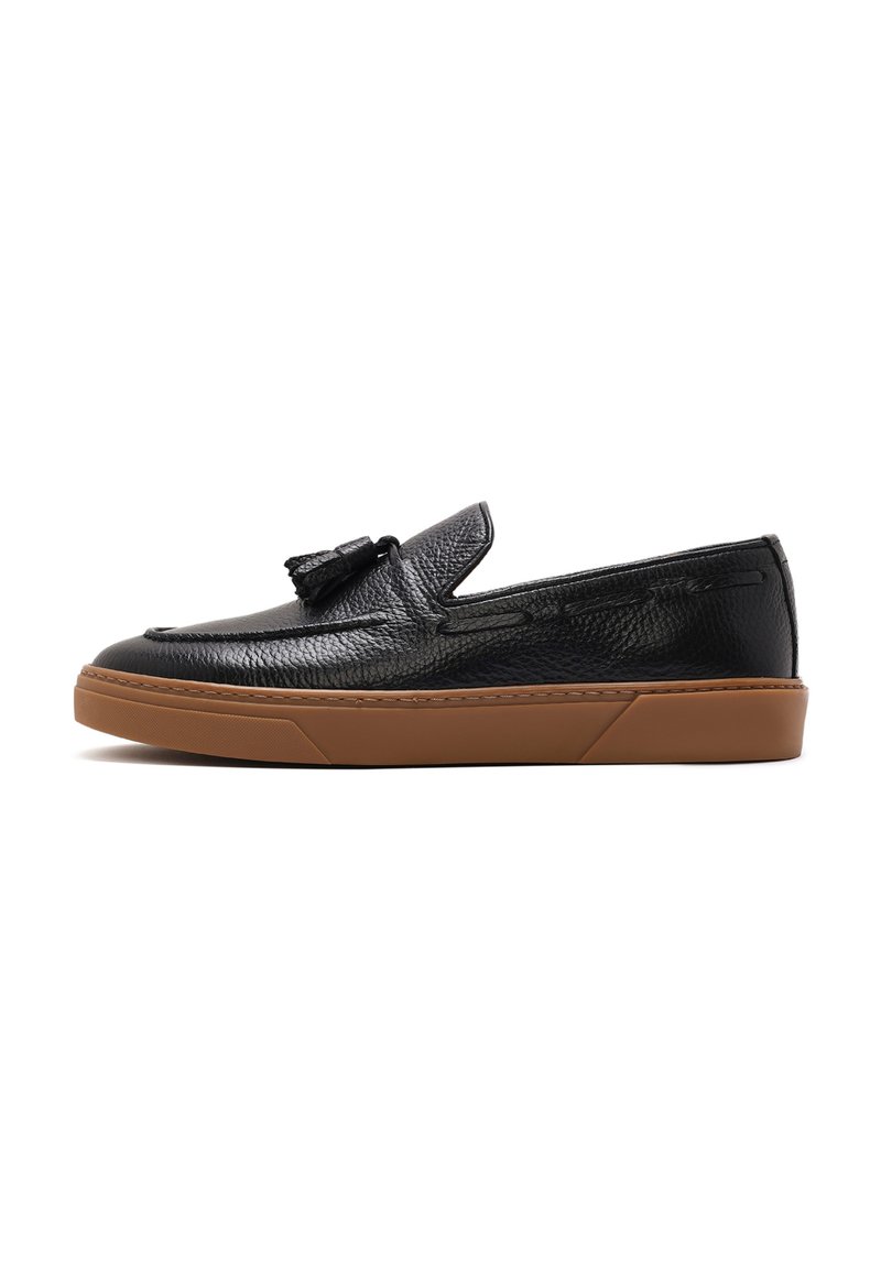 Scarpa nera in pelle slip-on con finitura texturizzata, dotata di un vezzoso nappino, punta arrotondata e suola in gomma marrone.