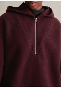 Bordowa bluza z kapturem z zamkiem na pół, wykonana z teksturowanej mieszanki wełny, z wyraźnym dekoltem w kształcie litery V.