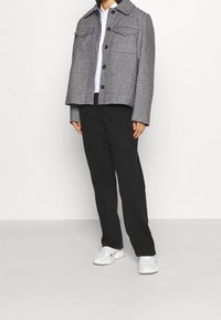 Chaqueta de cuadros en blanco y negro con dos bolsillos frontales, cierre de botones y collar puntiagudo, combinada con pantalones negros y zapatillas blancas.