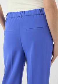Blå bukser med elastisk midje, glatt tekstur og to baklommer. Designet har rene linjer og en skreddersydd passform.