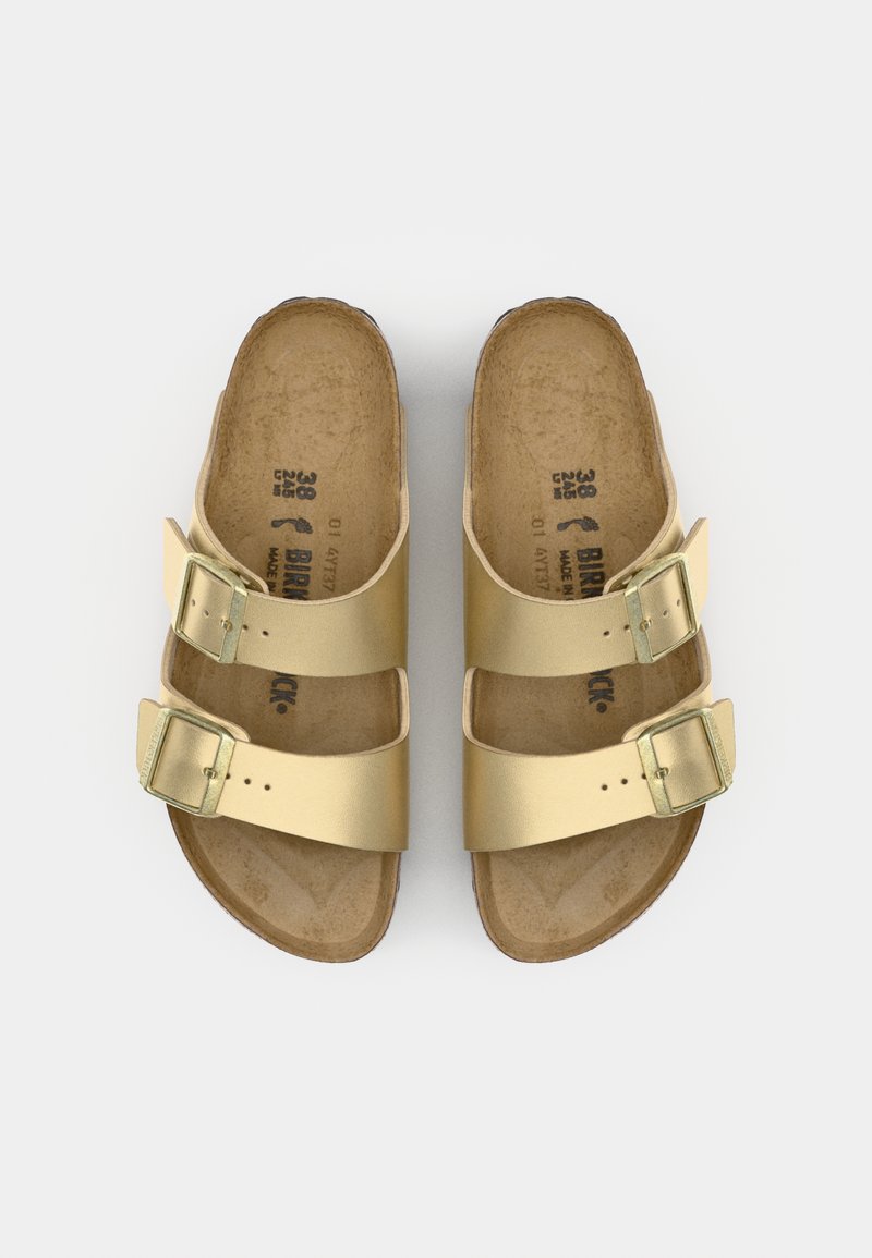 Goldene Sandalen mit zwei verstellbaren Riemen, metallischen Schnallen und einem Korkfußbett. Flache Sohle, offenes Zehendesign und minimalistischer Stil.