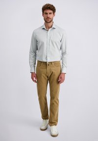 Hellblaues Button-Up-Hemd, khakifarbene Hose und weiße Turnschuhe. Slim Fit Design, glatte Textur und Ärmel in mittellänger.