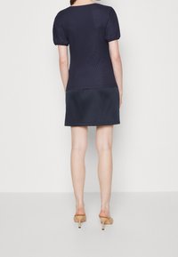 Námořnická halenka s texturou a balónovými rukávy, v kombinaci s hladkou námořnickou sukní. Tento outfit se vyznačuje hladkým materiálem a jednoduchou, přiléhavou siluetou.