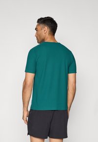 Türkises T-Shirt mit kurzen Ärmeln, gerippter Textur und Rundhalsausschnitt, kombiniert mit schwarzen Shorts. Das Design ist einfach und ungeschmückt.