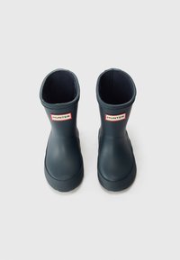 Bottes de pluie en caoutchouc bleu marine avec une surface lisse, à coupe basse et semelle texturée. Présente un logo "HUNTER" rouge et blanc à l'avant.
