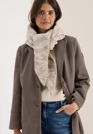 Beige gestrickter Schal mit strukturiertem Muster, über einem hellen Pullover getragen, ergänzt durch einen braunen Mantel und blaue Jeans.
