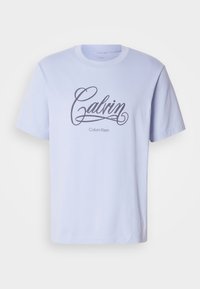 Jasnoniebieska bawełniana koszulka z krótkim rękawem, z logo "Calvin" w kursywie w kolorze czarnym oraz tekstem "Calvin Klein" poniżej.